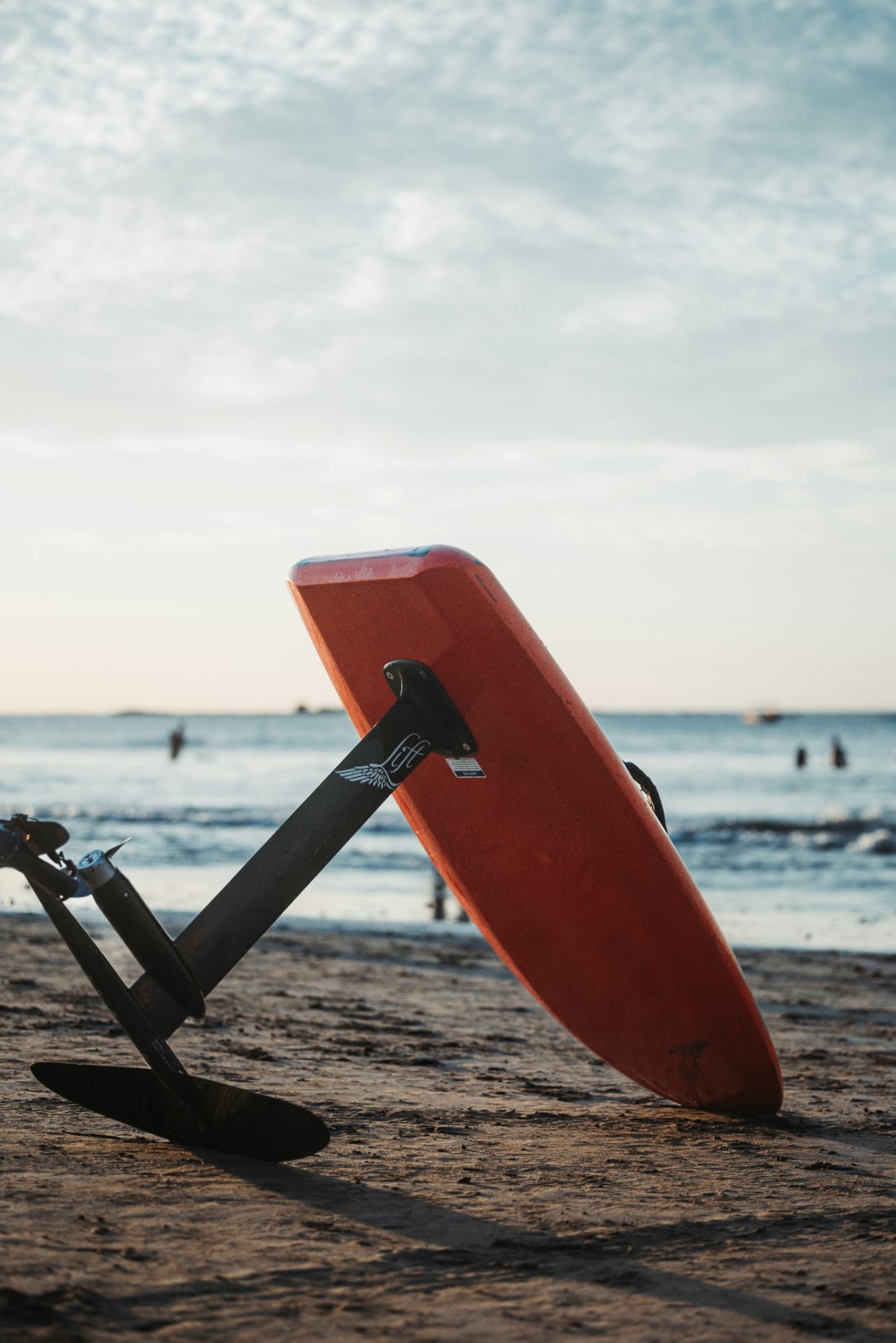 An e-foil board resting on its hydrofoil on the sand at dusk